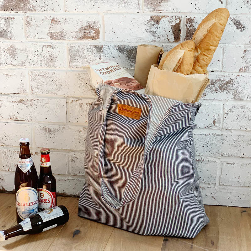 ダルトンの「ROUGHLY BAG（ラフリィバッグ）」は、荷物をガサッと詰め込める軽快なキャンバストート。柔らかい薄手生地で体に馴染み、サブバッグやエコバッグとしても大活躍。シンプルながら無骨なデザインは、ガレージやアウトドアのラフなシーンに最適です。